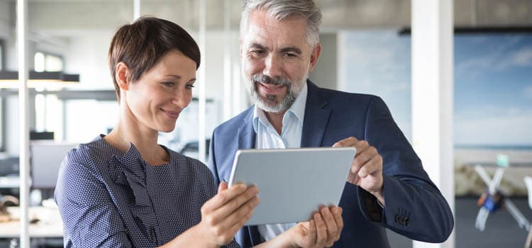 Eine Frau und ein Mann gucken erfreut etwas auf einem Tablet an.