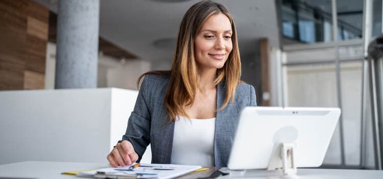 Eine Frau sitzt an einem Bildschirm, notiert sich etwas und lächelt.