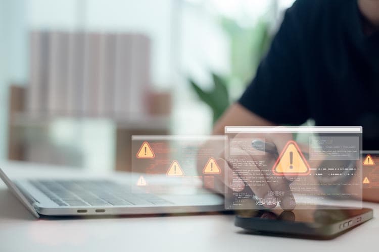 Eine Person benutzt ein Smartphone auf einem Schreibtisch mit Laptop, darüber "schweben" kleine Screens mit Warnhinweisen.