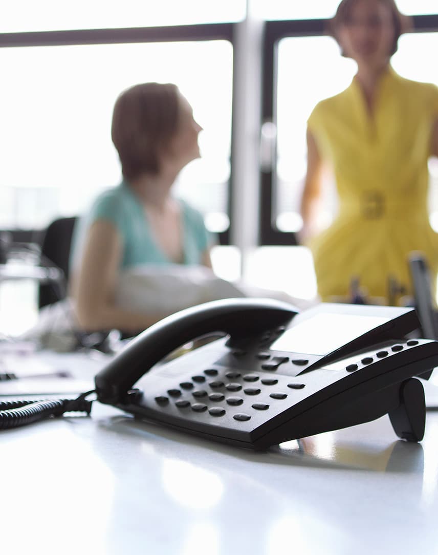 Telefonanlage, im Hintergrund zwei sich unterhaltende Kolleginnen