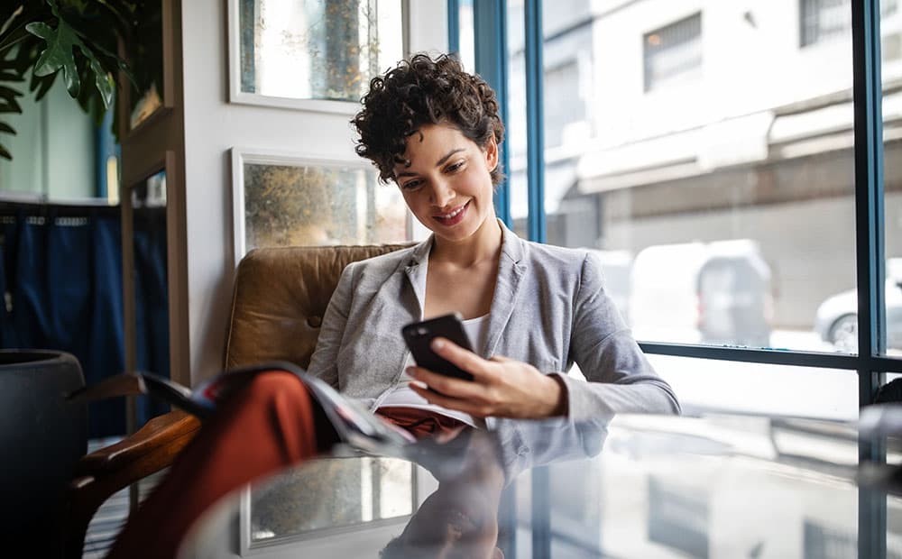 Frau im Business-Look im Café mit Smartphone in der Hand