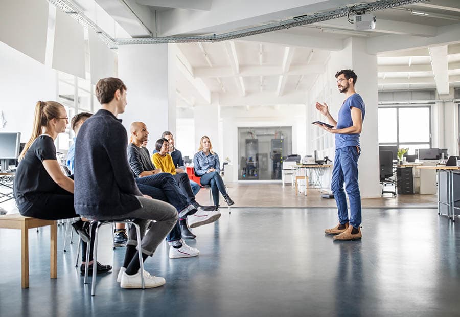 Eine Gruppe in einer Sitzrunde, daneben ein Seminarleiter