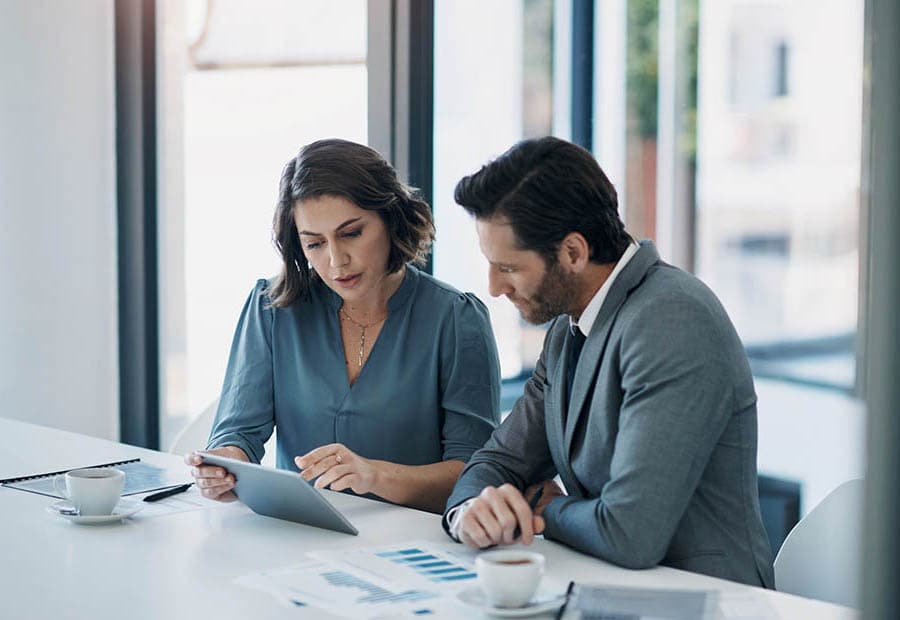 Ein Mann und eine Frau an einem Schreibtisch, die etwas auf einem Tablet prüfen