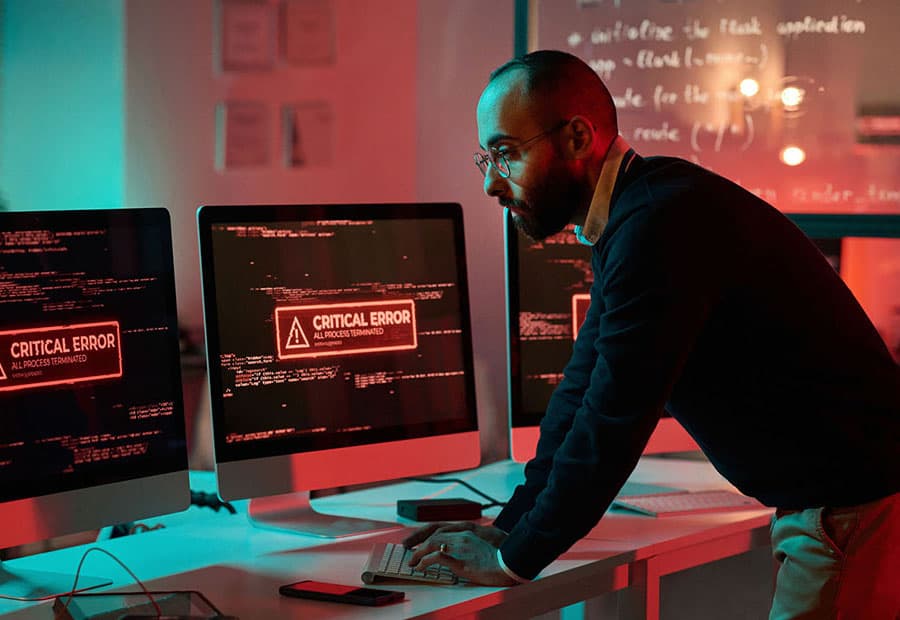 Ein Mitarbeiter vor zwei rot erleuchteten Bildschirmen, auf denen der Hinweis "Critical Error" zu lesen ist