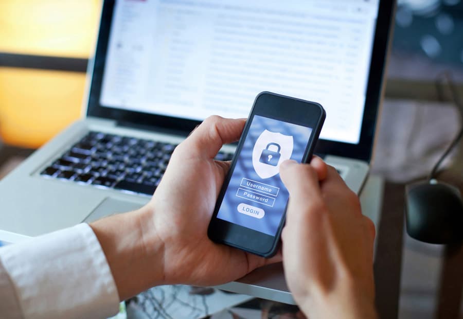 Ein Smartphone mit einer Login-Aufforderung, dahinter ein Laptop