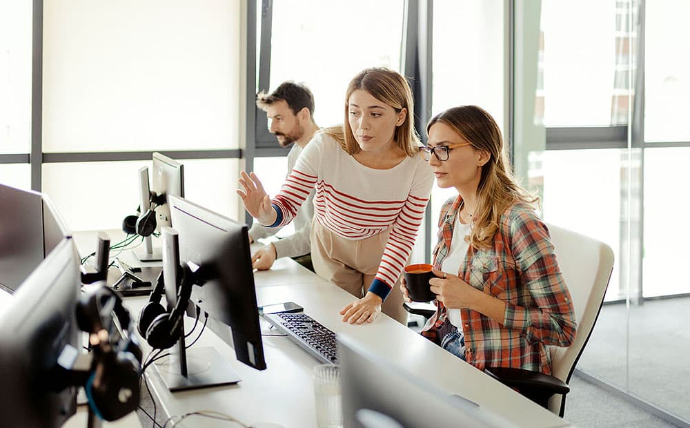 Zwei junge Frauen, die in einem Büro an einem Computerbildschirm etwas besprechen