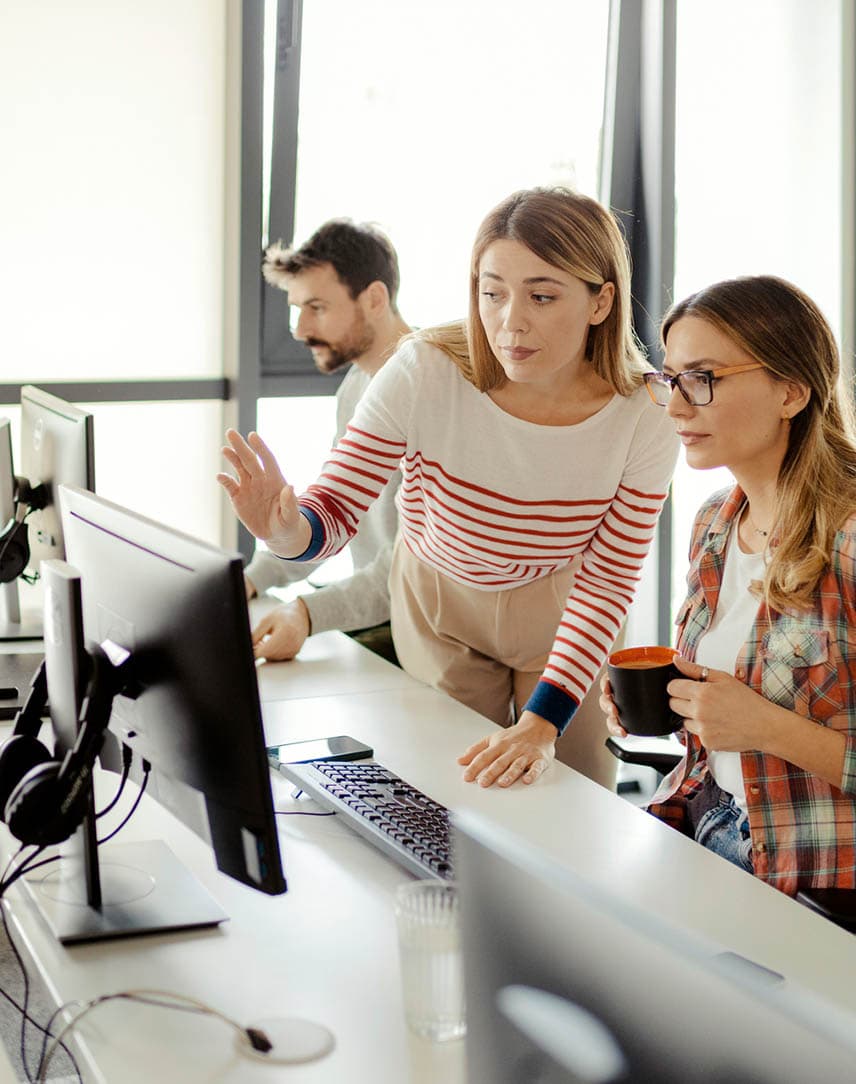 Zwei junge Frauen, die in einem Büro an einem Computerbildschirm etwas besprechen