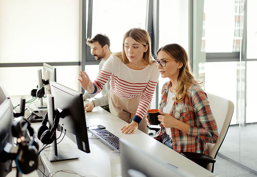 Zwei junge Frauen, die in einem Büro an einem Computerbildschirm etwas besprechen