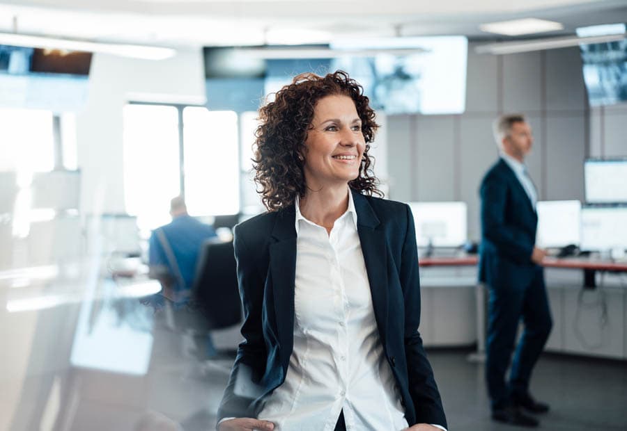Eine Frau steht in einem Kontrollraum und lächelt.