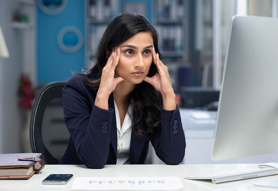 Eine Geschäftsfrau guckt auf Ihren Bildschirm und hält sich die Schläfen.