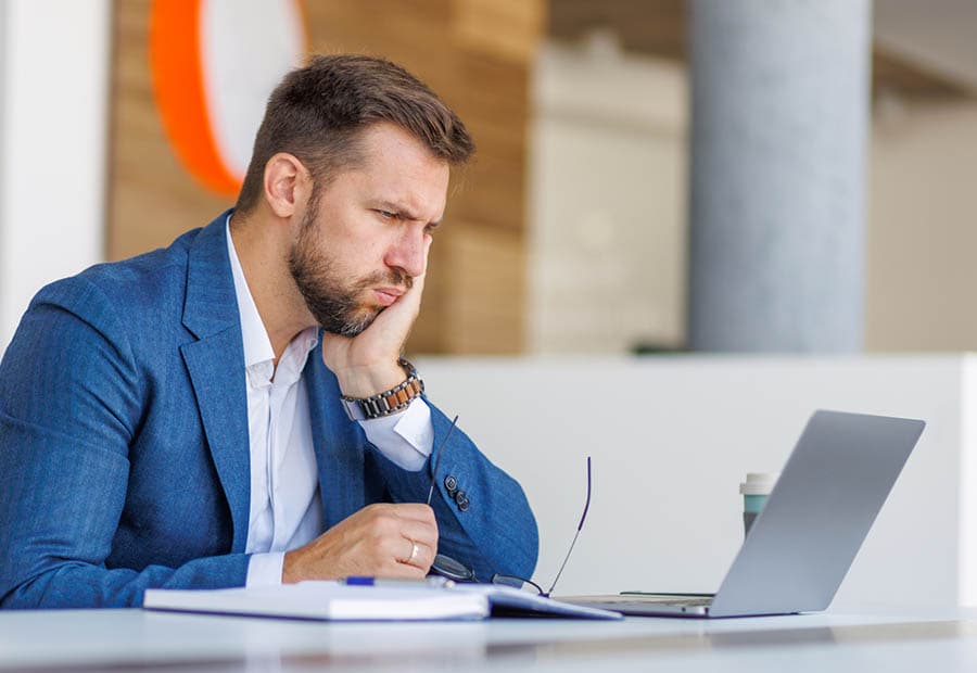 Ein Geschäftsmann guckt auf seinen Laptop und stützt den Kopf in die linke Hand.