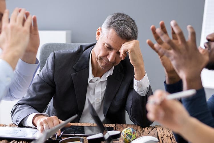 Nachdenklicher Geschäftsmann an einem Besprechungstisch zwischen argumentierenden Kollegen
