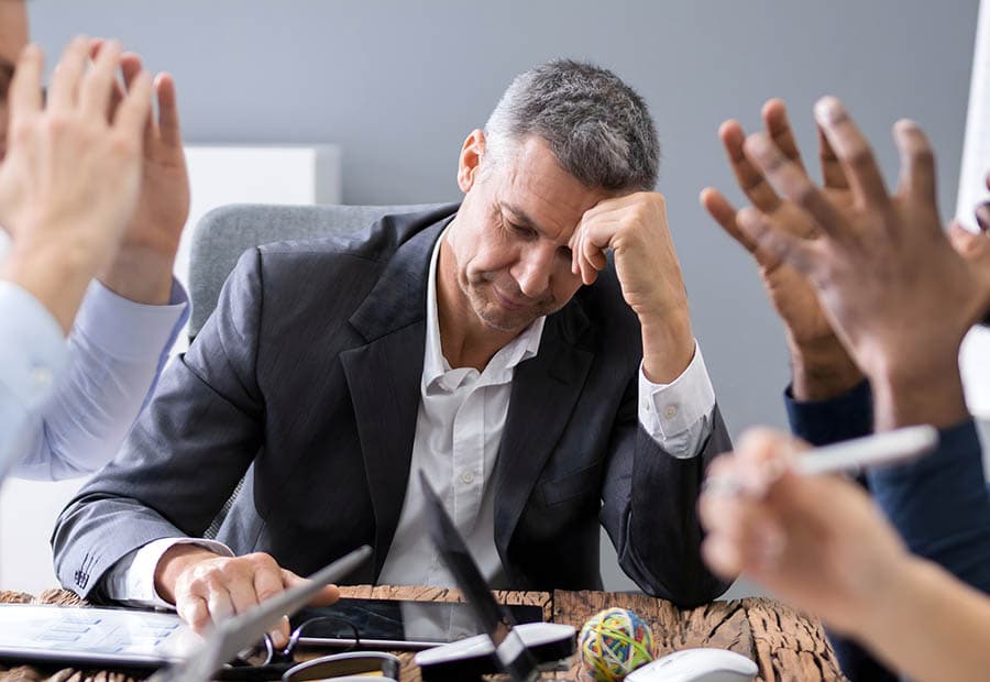 Nachdenklicher Geschäftsmann an einem Besprechungstisch zwischen argumentierenden Kollegen