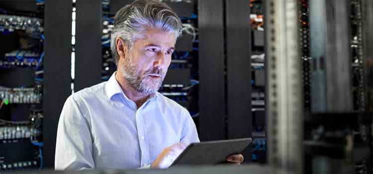 Ein Mann mit Tablet prüft etwas an einem Serverschrank.