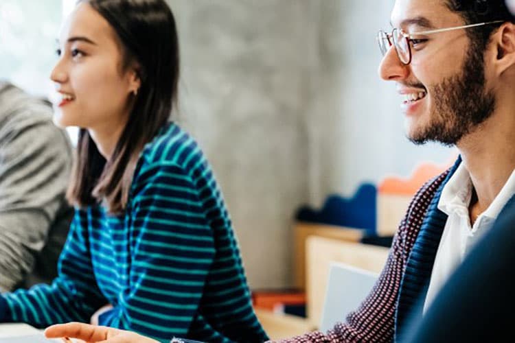 Schülerinnen und Schüler sitzen in einem Klassenzimmer vor Laptops.