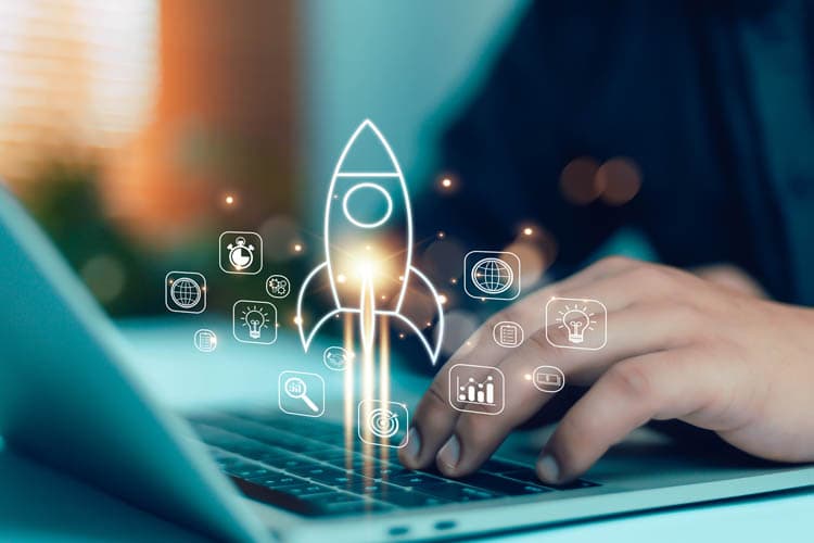 Eine Person arbeitet an einem Laptop, darauf ist das Icon einer startenden Rakete sowie andere kleinere Icons zu sehen, die zur digitalen Arbeit passen.