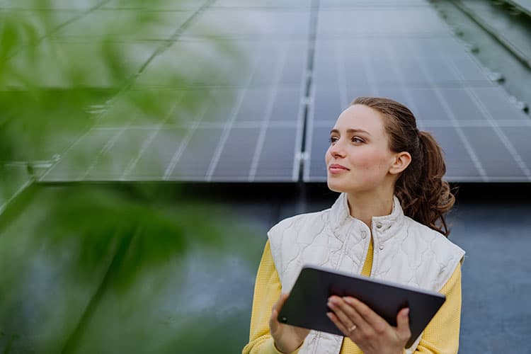 Eine Frau mit Tablet steht vor einer PV-Anlage und lächelt.