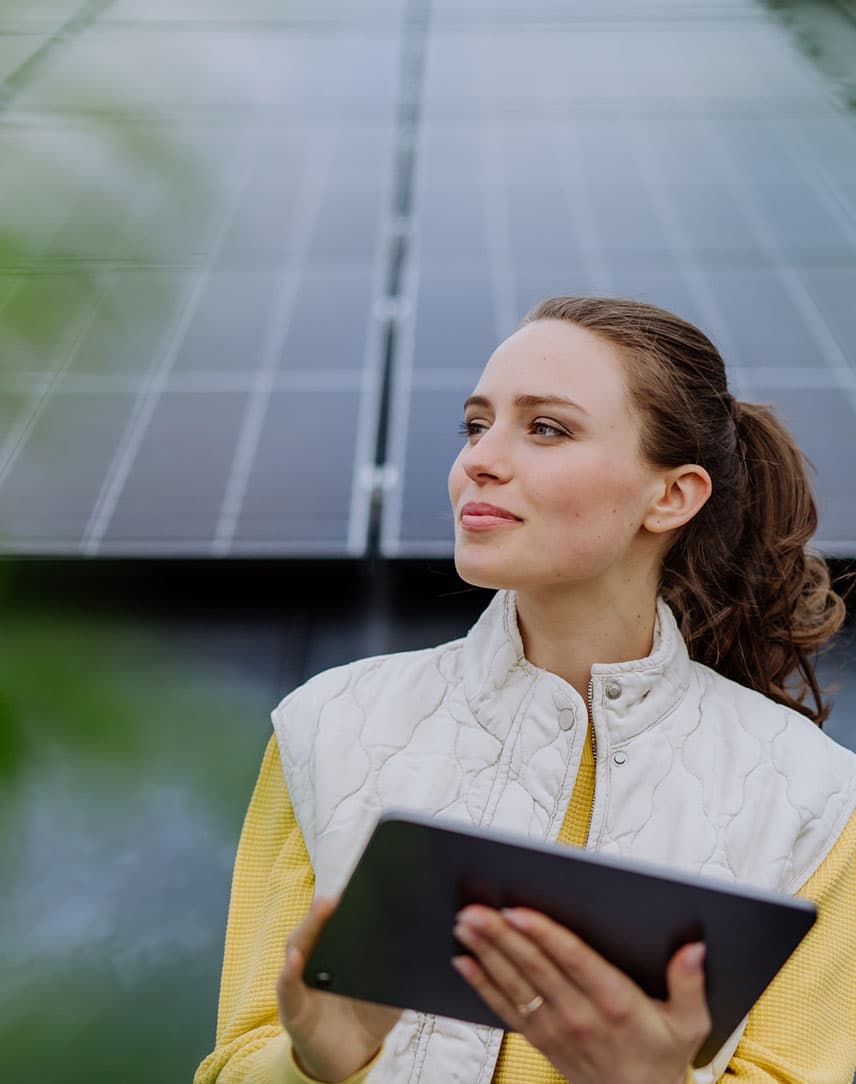 Eine Frau mit Tablet steht vor einer PV-Anlage und lächelt.