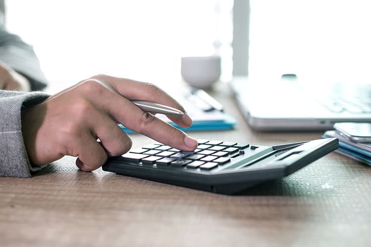 Eine Hand, die etwas auf einem Taschenrechner eingibt, der auf einem Schreibtisch liegt