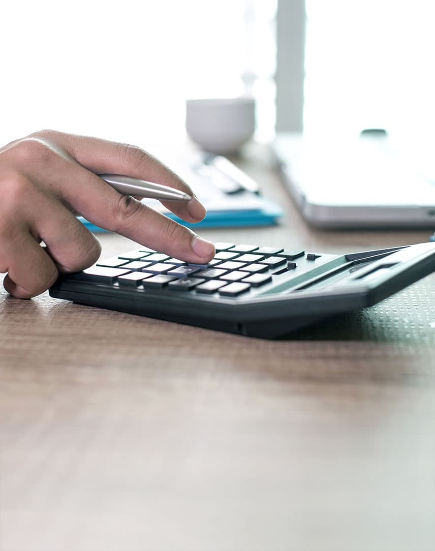 Eine Hand, die etwas auf einem Taschenrechner eingibt, der auf einem Schreibtisch liegt