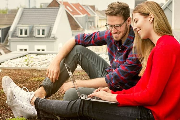 Paar sitzt auf einer Dachterrasse und schaut auf einen Laptop