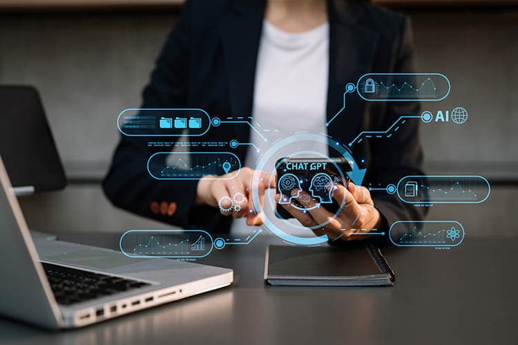 Eine Frau im schwarzen Blazer sitzt vor einem Laptop, im Vordergrund hellblau stilisierte Symbole für Künstliche Intelligenz