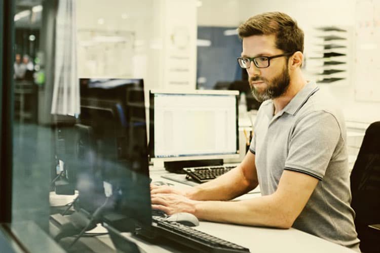 Ein Mann sitzt in einem Büro an einem Schreibtisch, schaut auf einen Monitor und arbeitet.