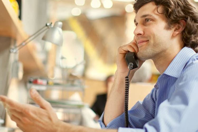 Ein junger Mann sitzt an seinem Arbeitsplatz und telefoniert mit seinem Telefon.