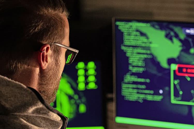 Ein Cyberkrimineller sitzt vor zwei Bildschirmen und plant seinen nächsten Phishing-Angriff auf ein Unternehmen.