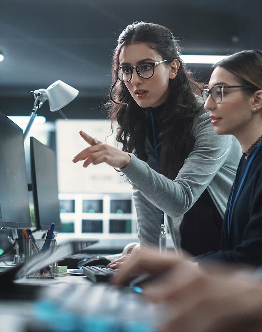 Zwei Mitarbeitende prüfen etwas auf Bildschirmen.