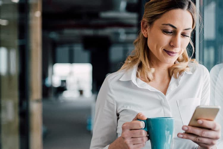 Eine Frau lehnt an einer Glasfassade und guckt auf ihr Smartphone