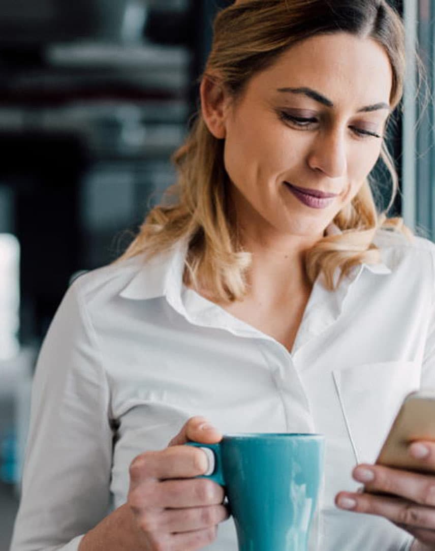 Eine Frau lehnt an einer Glasfassade und guckt auf ihr Smartphone