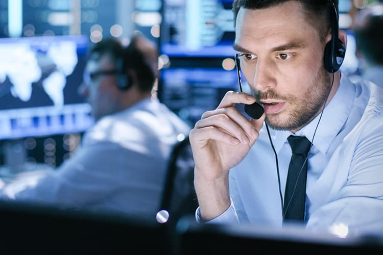 Ein Mann spricht in einem blau erleuchteten Kontrollraum in ein Headset