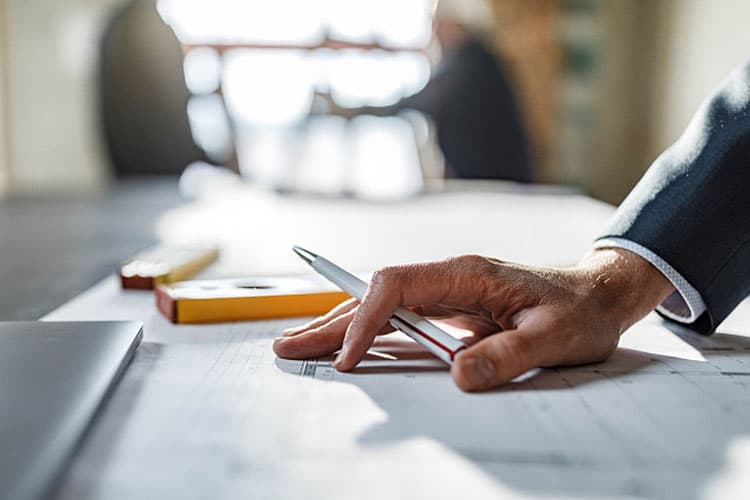 Eine Hand mit Kuli, die sich auf einen Bauplan abstützt
