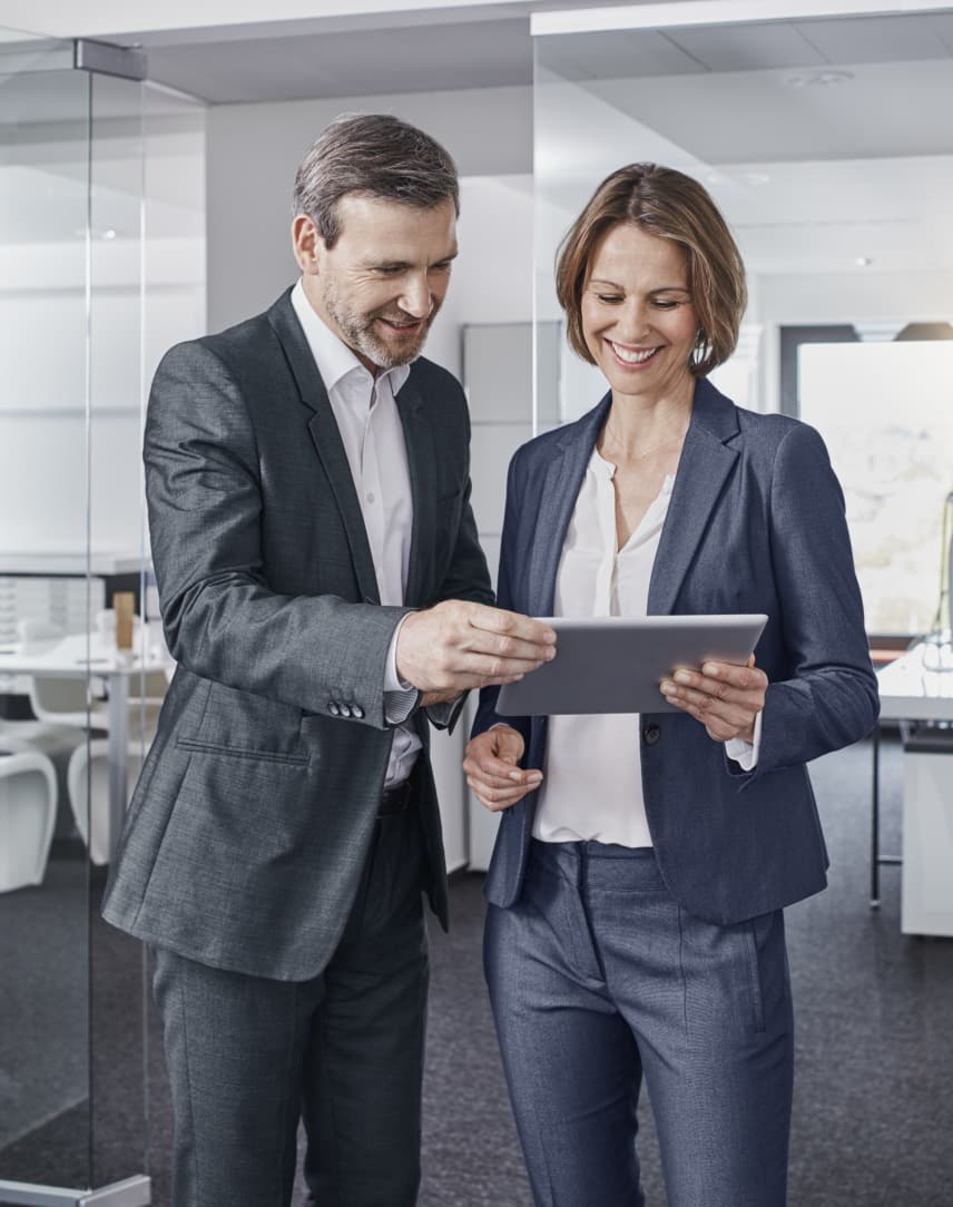 Eine Frau und ein Mann gucken in einem Büro auf ein Tablet.