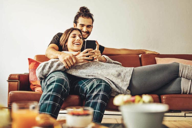 Eine Frau und ein Mann auf einem Sofa, die über etwas auf einem Smartphone lachen