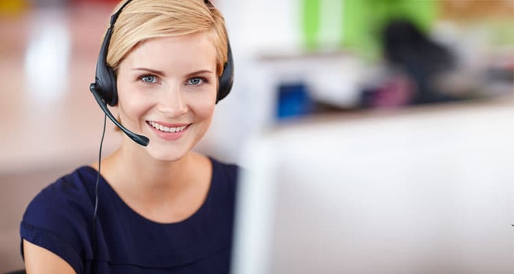 Eine lächelnde Frau mit Headset vor einem Arbeitsbildschirm