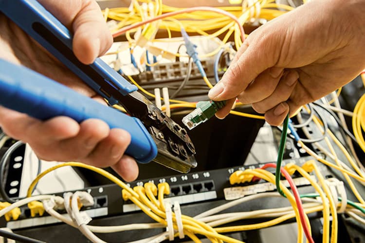 Zwei Hände mit Zange und Kabel werkeln an einem Server