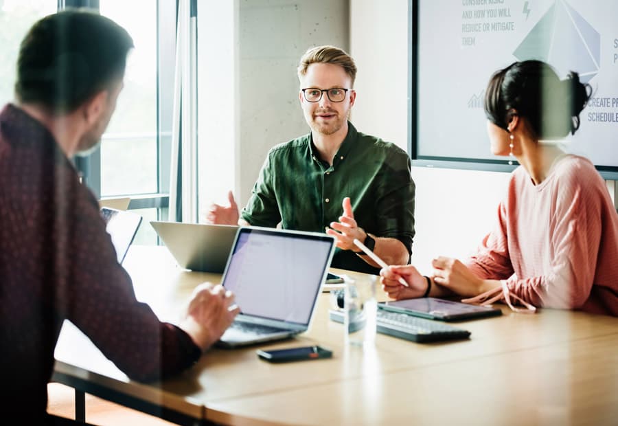 Drei Personen an einem Arbeitstisch mit Laptops