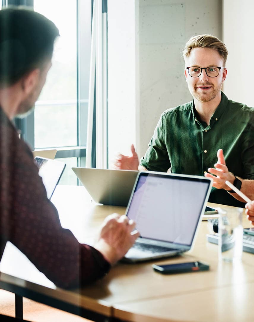 Ein Mann im grünen Hemd, der mit zwei Kolleg*innen etwas an einem Meetingtisch bespricht