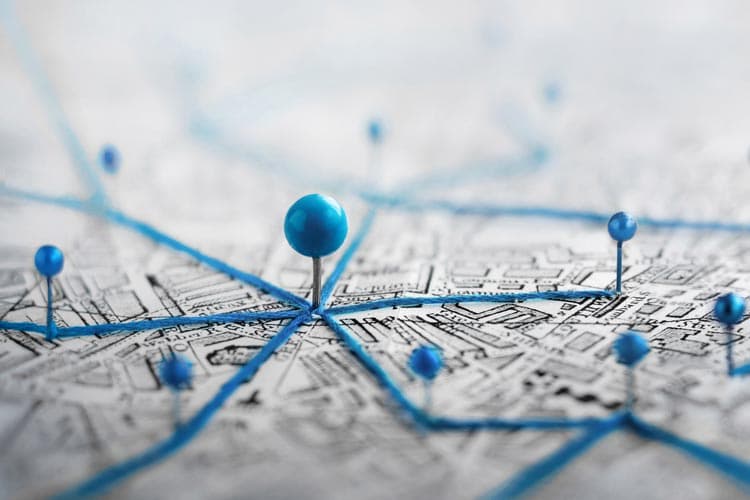 Ein Stadtplan mit stilisierten blauen Stecknadeln, die per blauen Fäden verbunden sind und eine Vernetzung symbolisieren