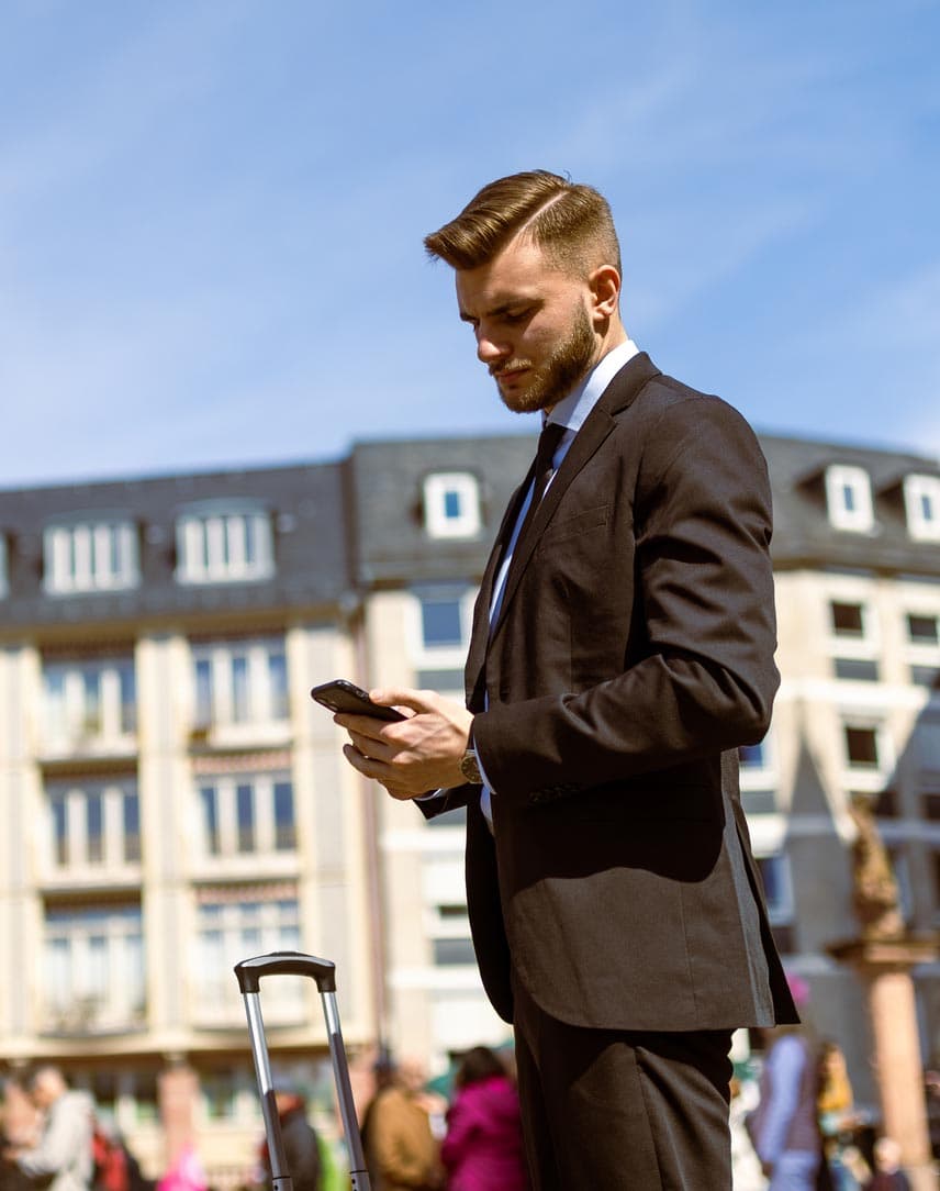 Ein junger Mann im Anzug steht auf einem urbanen Platz und guckt auf seine Smartphone.