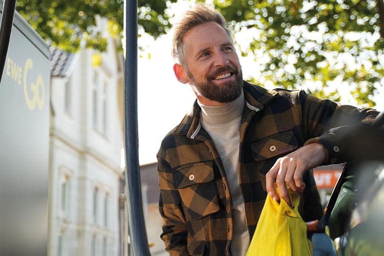 Ein Mann mit Flanelljacke steht an einem E-Auto, das er an einer EWE-Go-Ladestation lädt.