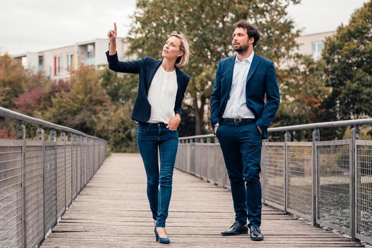 Eine Frau und ein Mann in Business-Kleidung, die auf einer Brücke stehen, die Frau deutet auf etwas