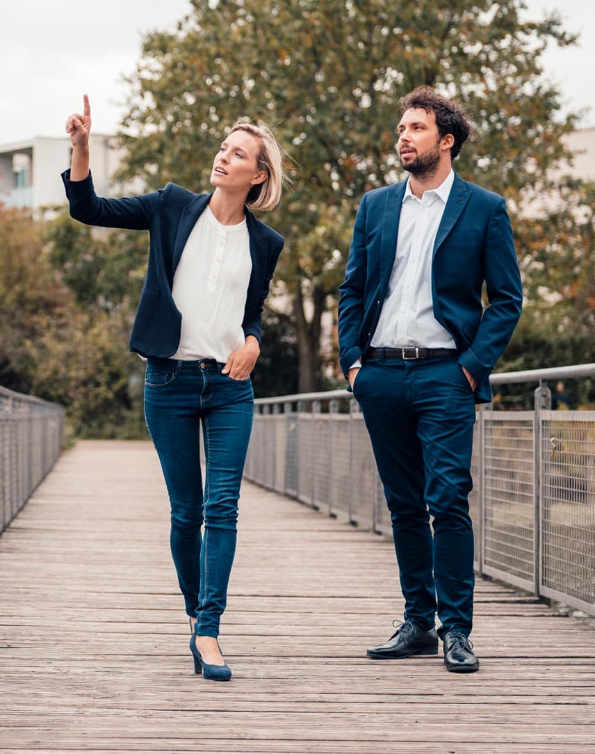 Eine Frau und ein Mann in Business-Kleidung, die auf einer Brücke stehen, die Frau deutet auf etwas