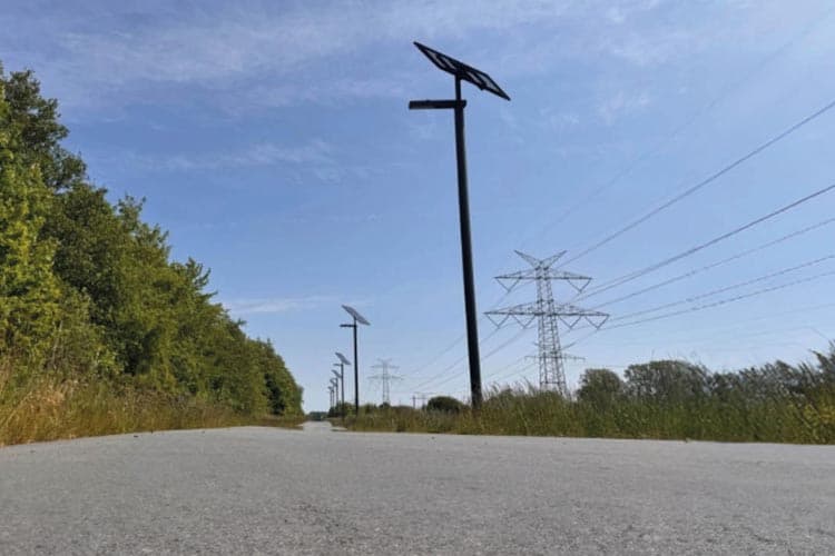 Solarleuchten an einem Straßenrand, dahinter Strommasten