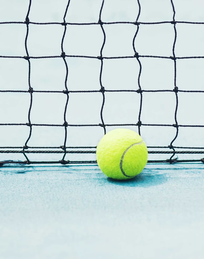 Ein gelber Tennisball liegt vor einem Tennisnetz