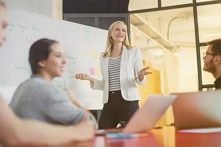 Eine Frau erklärt Erwachsenen etwas mithilfe eines Whiteboards.