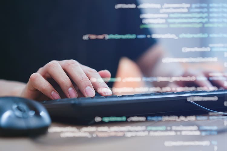 Eine Person arbeitet mit einer Tastatur, im Vordergrund Spiegelungen eines Bildschirms.