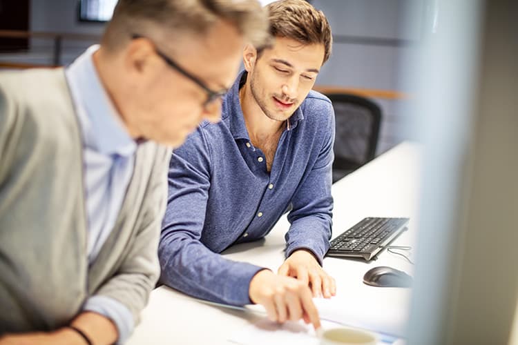 Zwei Männer unterhalten sich an einem digitalen Arbeitsplatz.
